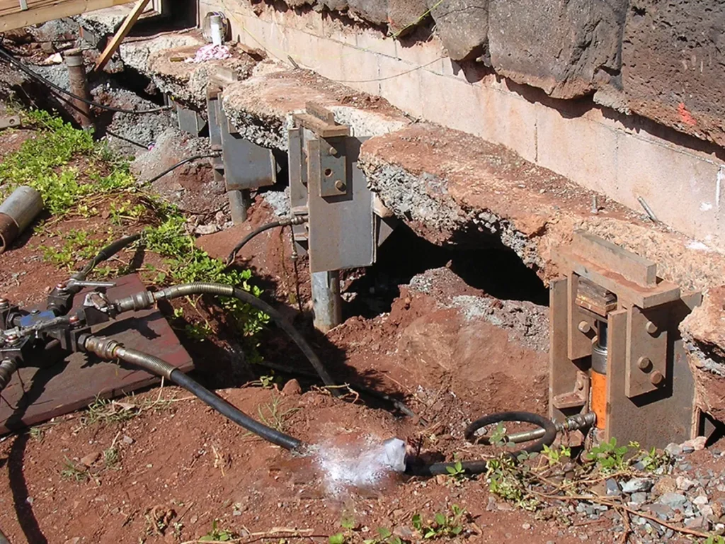 Structural Systems Hawaii hydraulic jacks and steel brackets releveling foundation piers on hillside home.