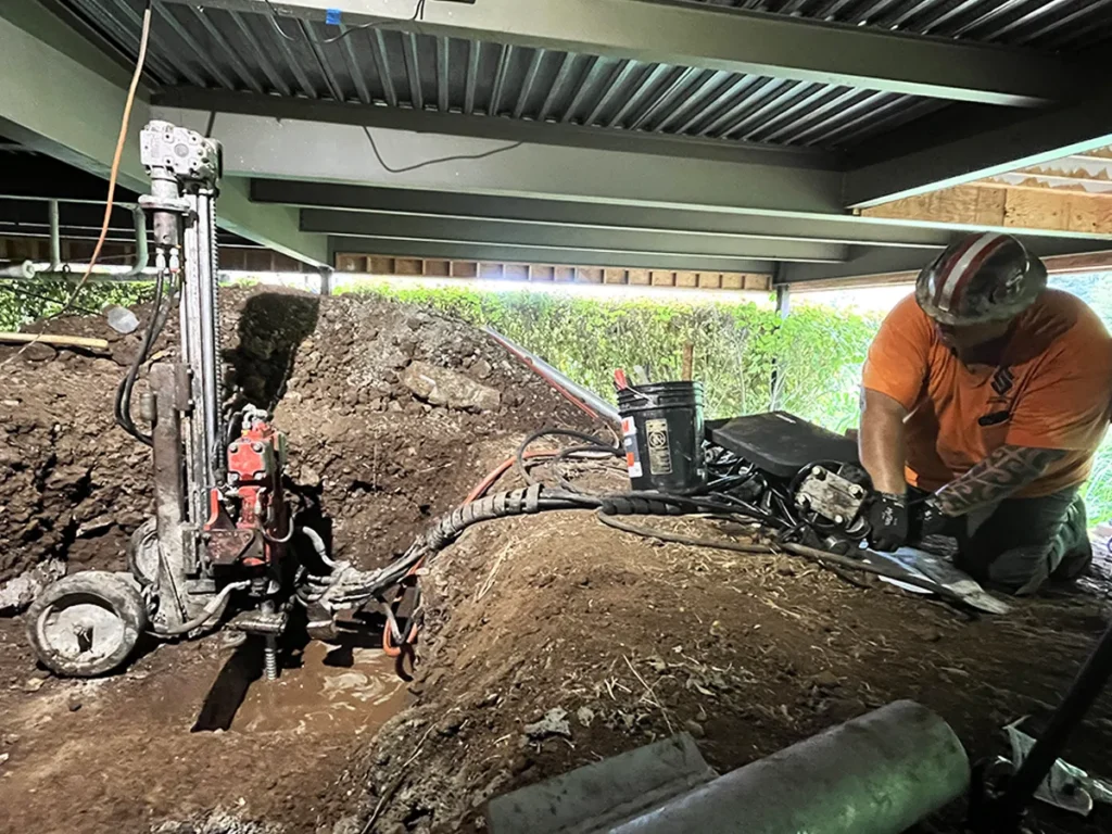 Structural Systems Hawaii technician drilling micropile underpinning system in home crawl space.